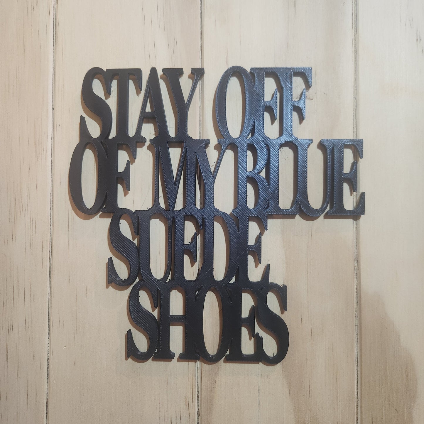 Black PLA 'Stay Off Of My Blue Suede Shoes' 3D printed wall art sign mounted on whitewashed wood wall, chunky serif lettering
