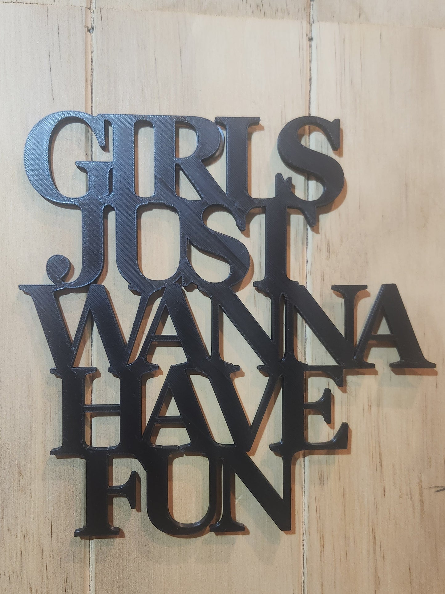 3D printed black PLA wall art sign reading Girls Just Wanna Have Fun in chunky stacked serif letters, mounted on a whitewashed wood wall, matte black finish, handmade in New Zealand