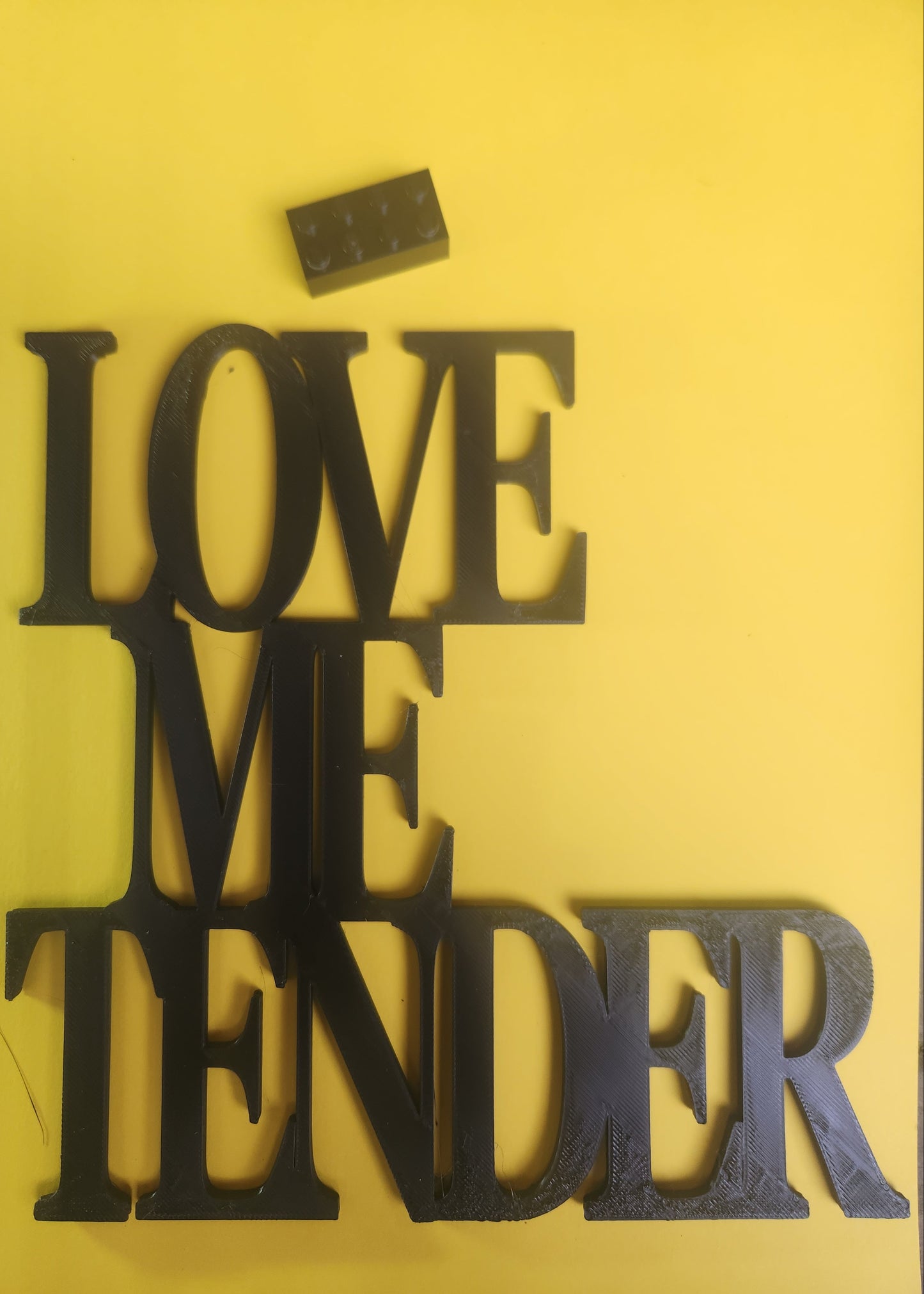 Love Me Tender sign in yellow with a Lego brick for scale, showing the size is approximately 19cm × 19cm