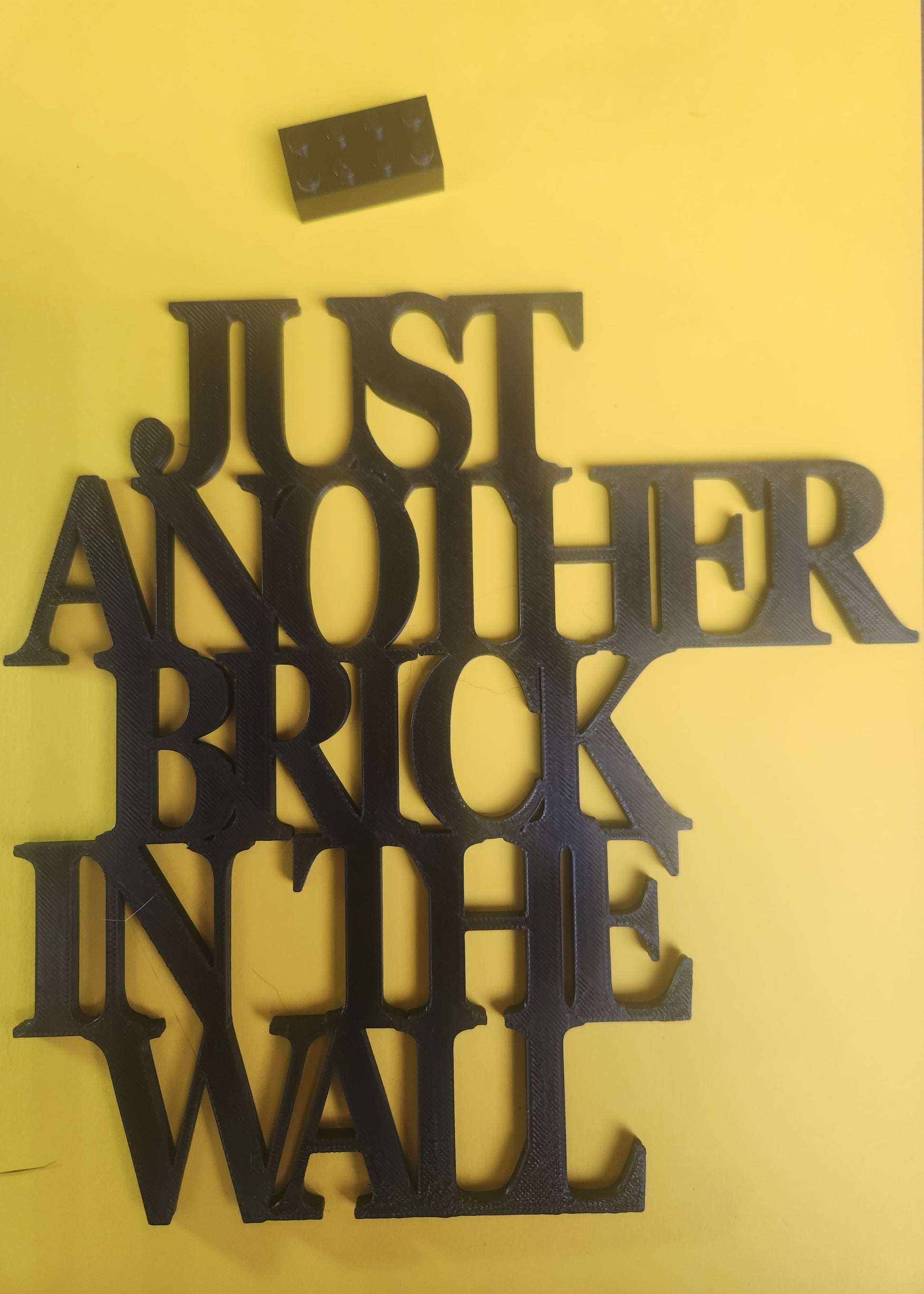 Just Another Brick in the Wall 3D printed sign with Lego brick for size scale, chunky serif lettering detail
