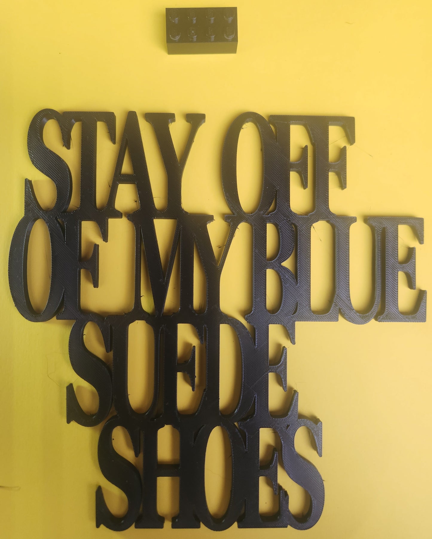 Black PLA 'Stay Off Of My Blue Suede Shoes' wall art sign on yellow background with Lego brick for scale, showing 19cm × 19cm size