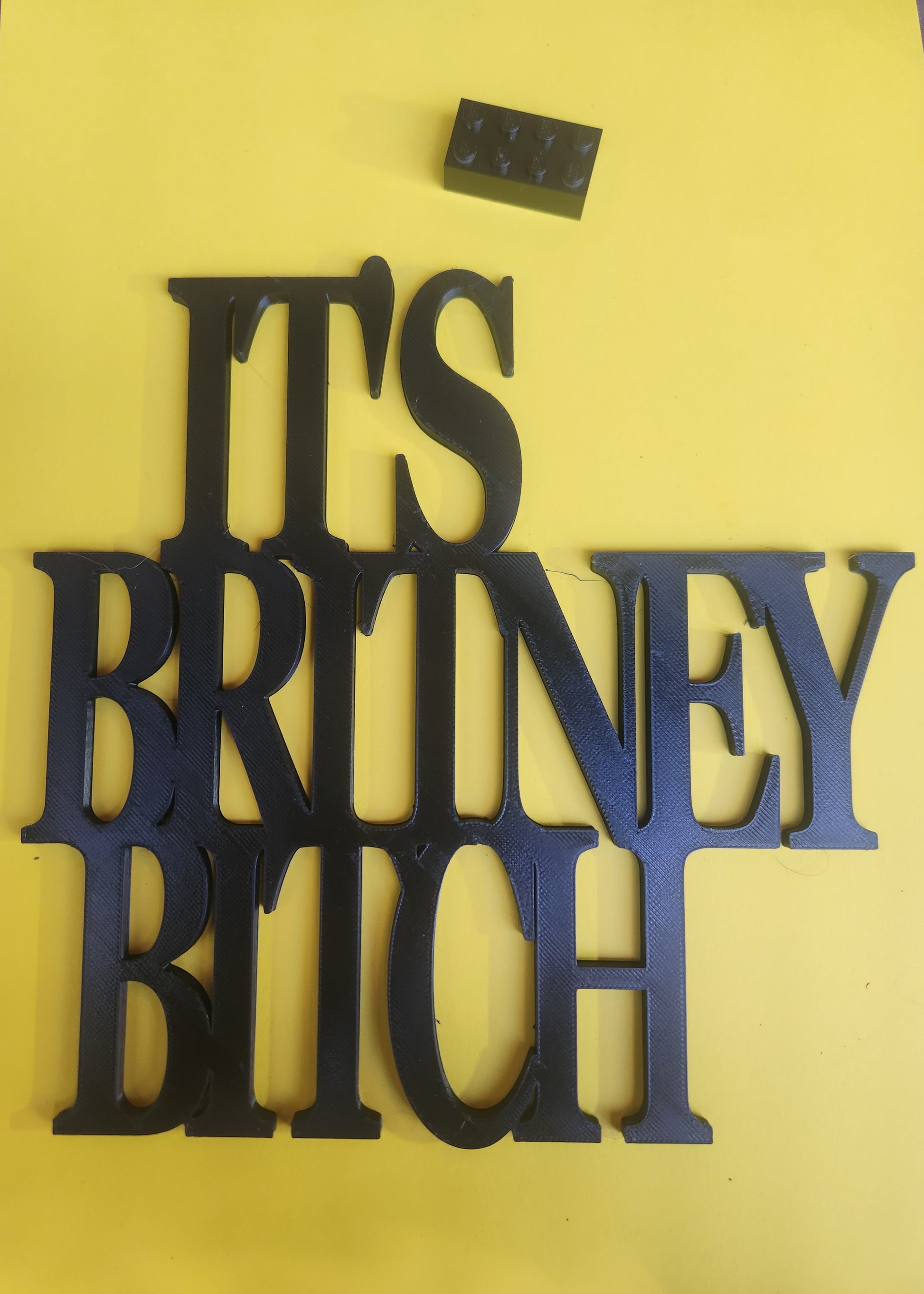 It's Britney B*tch 3D printed wall sign in black, shown next to Lego brick for size scale