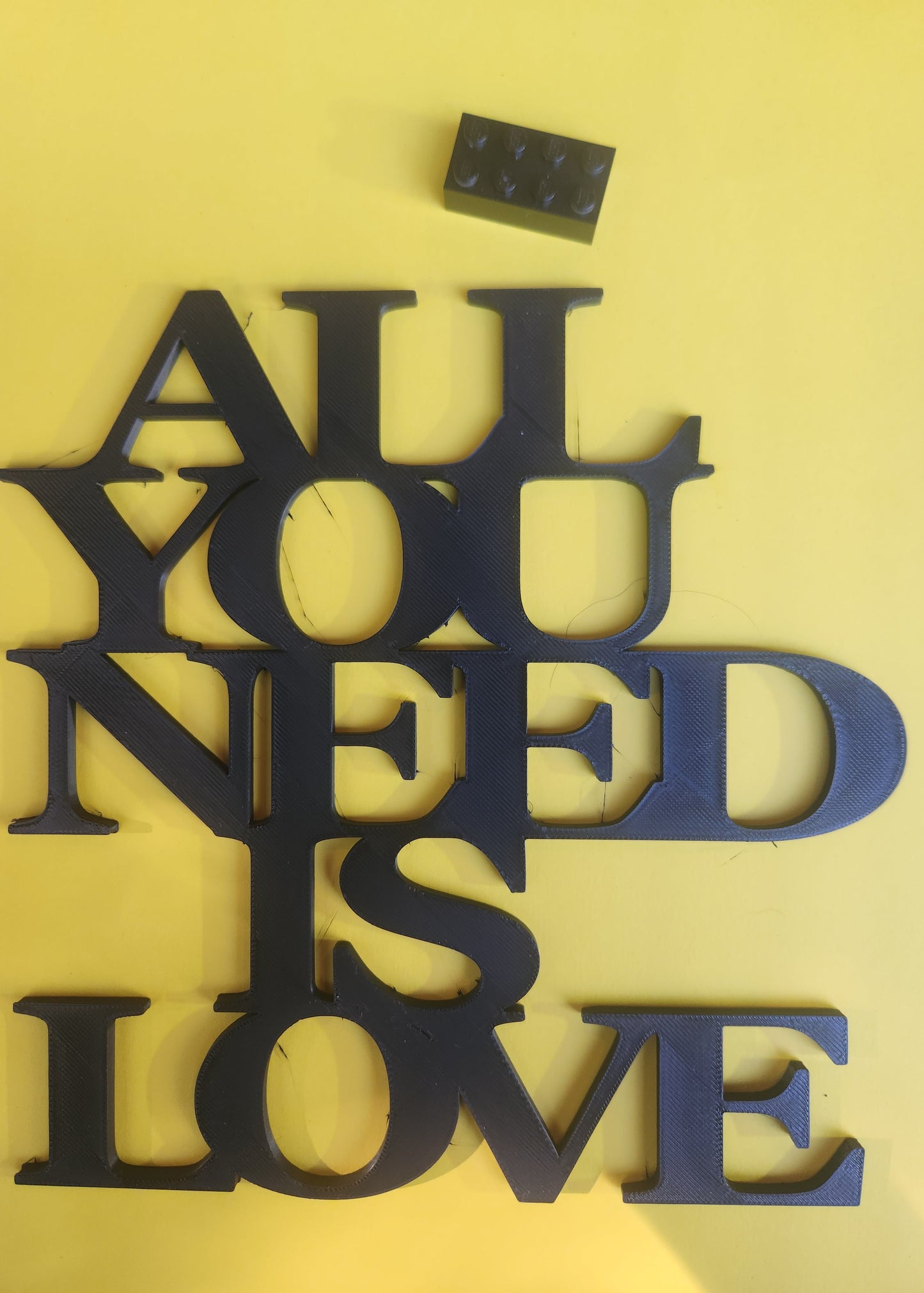 All You Need Is Love 3D printed sign next to a Lego brick for size reference, showing the compact 19cm × 19cm dimensions