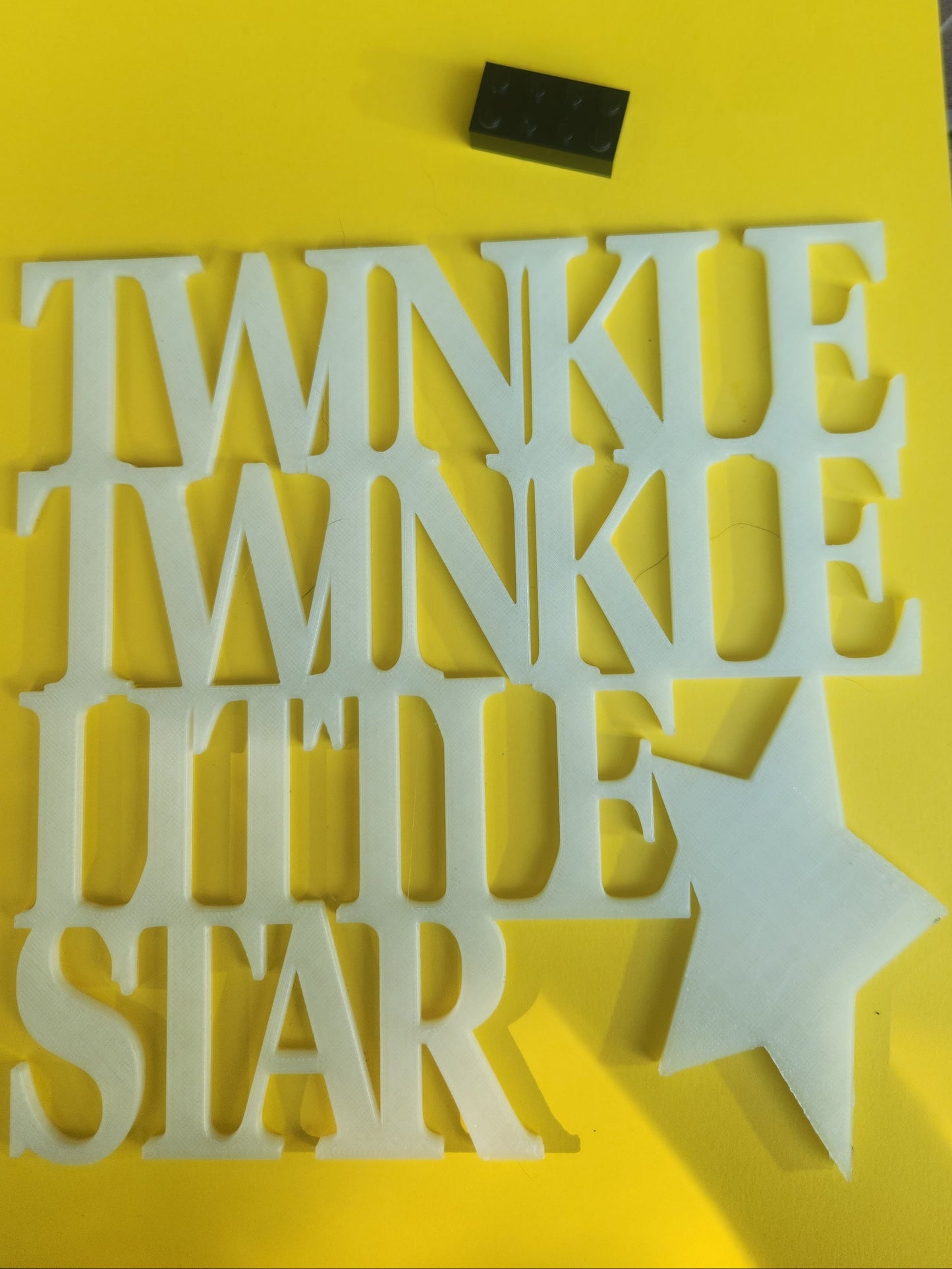  Twinkle Twinkle Little Star 3D printed glow in the dark PLA wall art sign shown flat on a yellow background with a Lego brick for scale, chunky stacked serif lettering with star, 19cm x 19cm, made in NZ