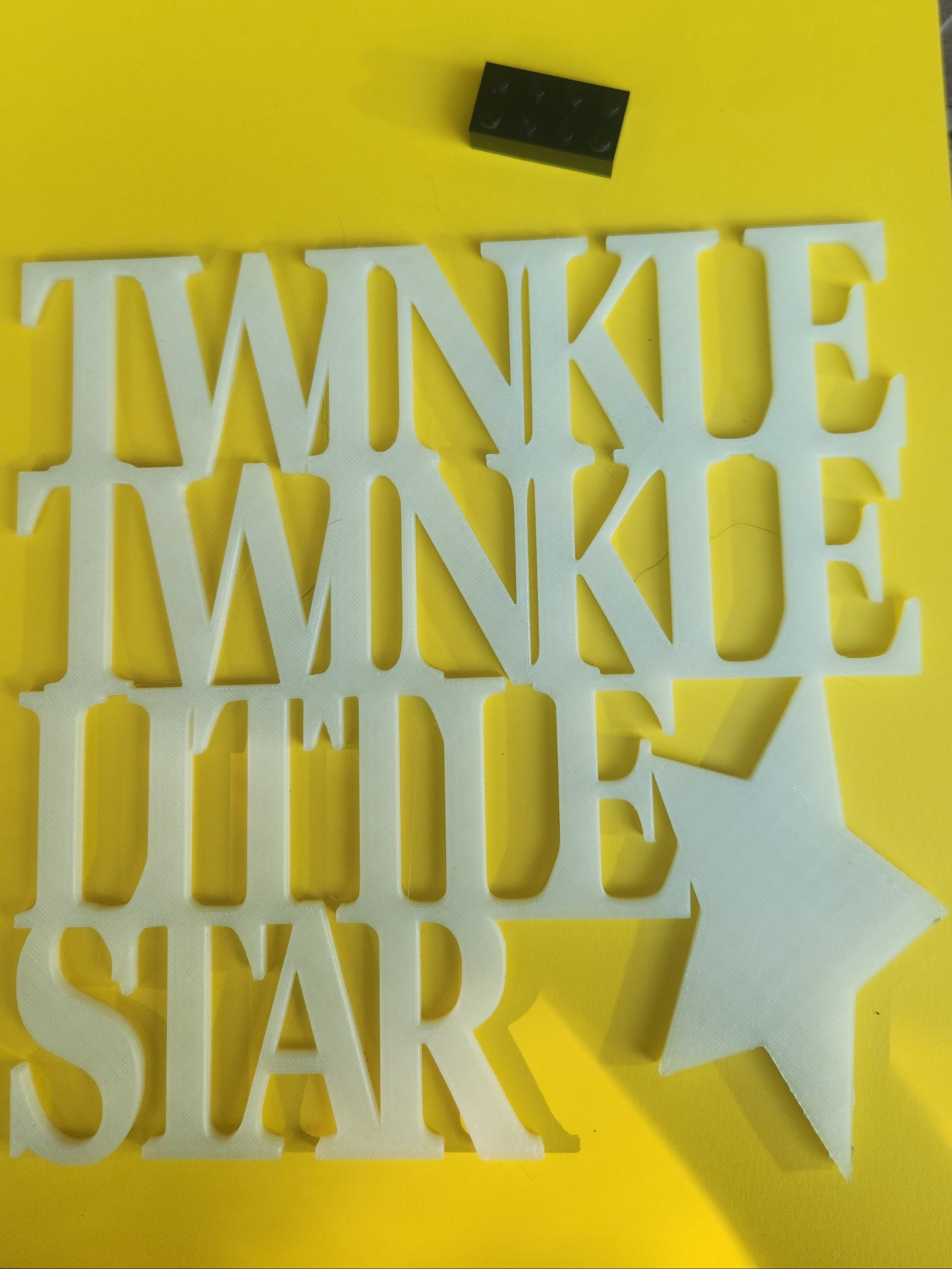  Twinkle Twinkle Little Star 3D printed glow in the dark PLA wall art sign shown flat on a yellow background with a Lego brick for scale, chunky stacked serif lettering with star, 19cm x 19cm, made in NZ