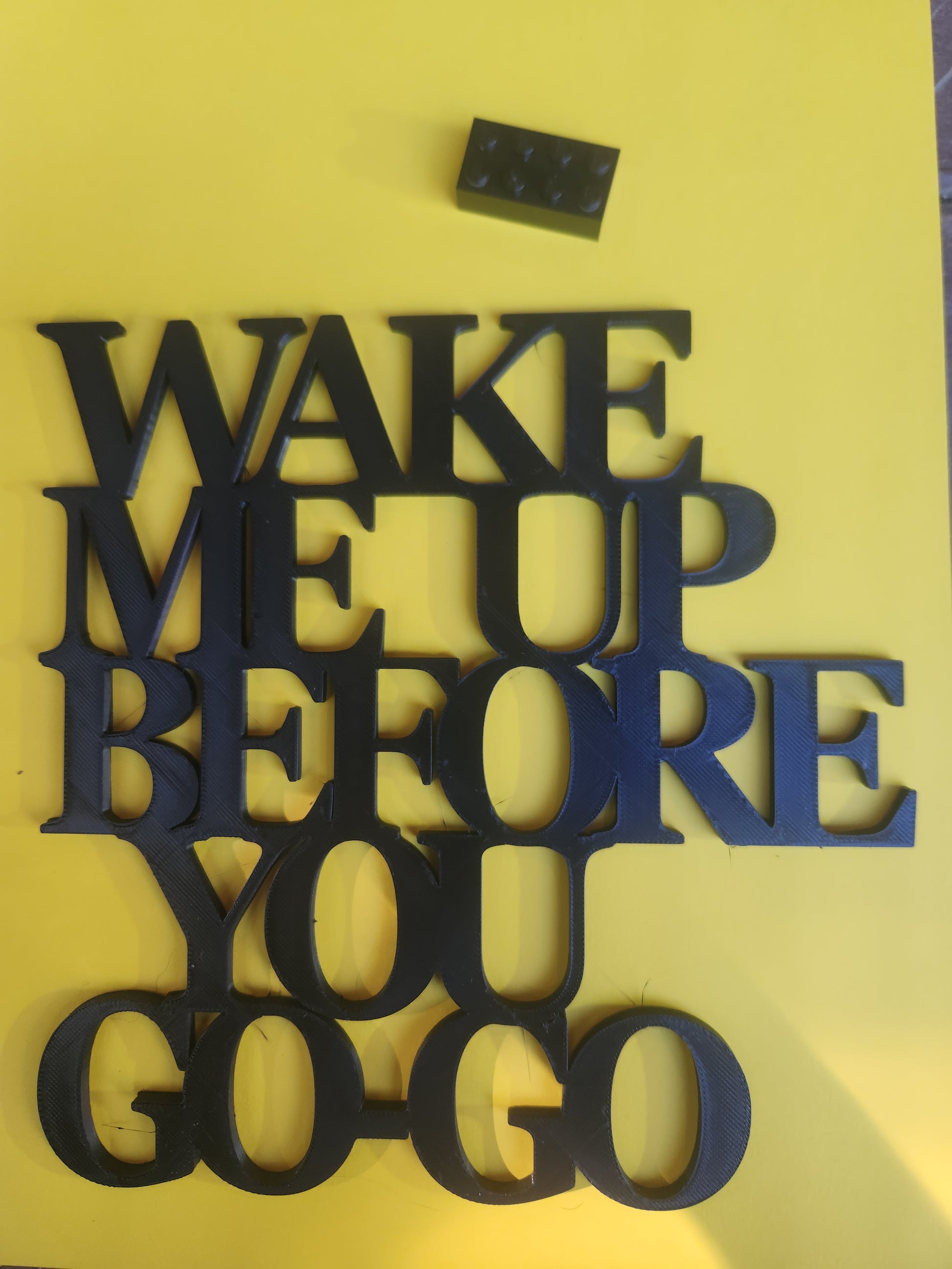 Wake Me Up Before You Go-Go 3D printed wall art sign in black PLA on yellow background with Lego brick for scale