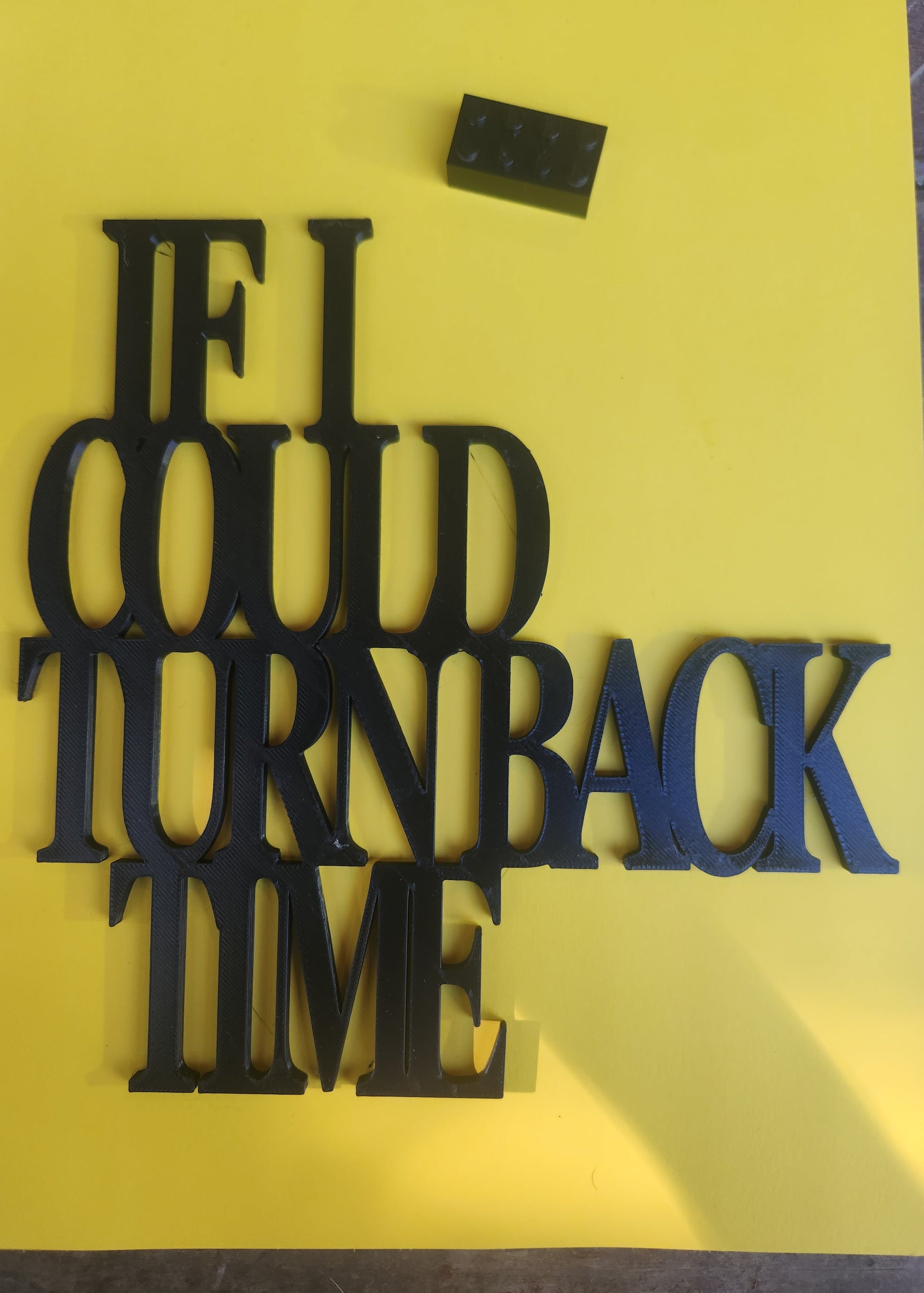 If I Could Turn Back Time wall art sign in black PLA, photographed on a yellow background next to a Lego brick for scale