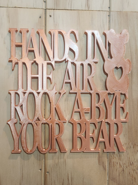 3D printed rose gold PLA wall art sign reading Hands in the Air Rock-A-Bye Your Bear with teddy bear silhouette, mounted on a whitewashed wood wall, 190mm x 190mm, handmade in Upper Hutt New Zealand