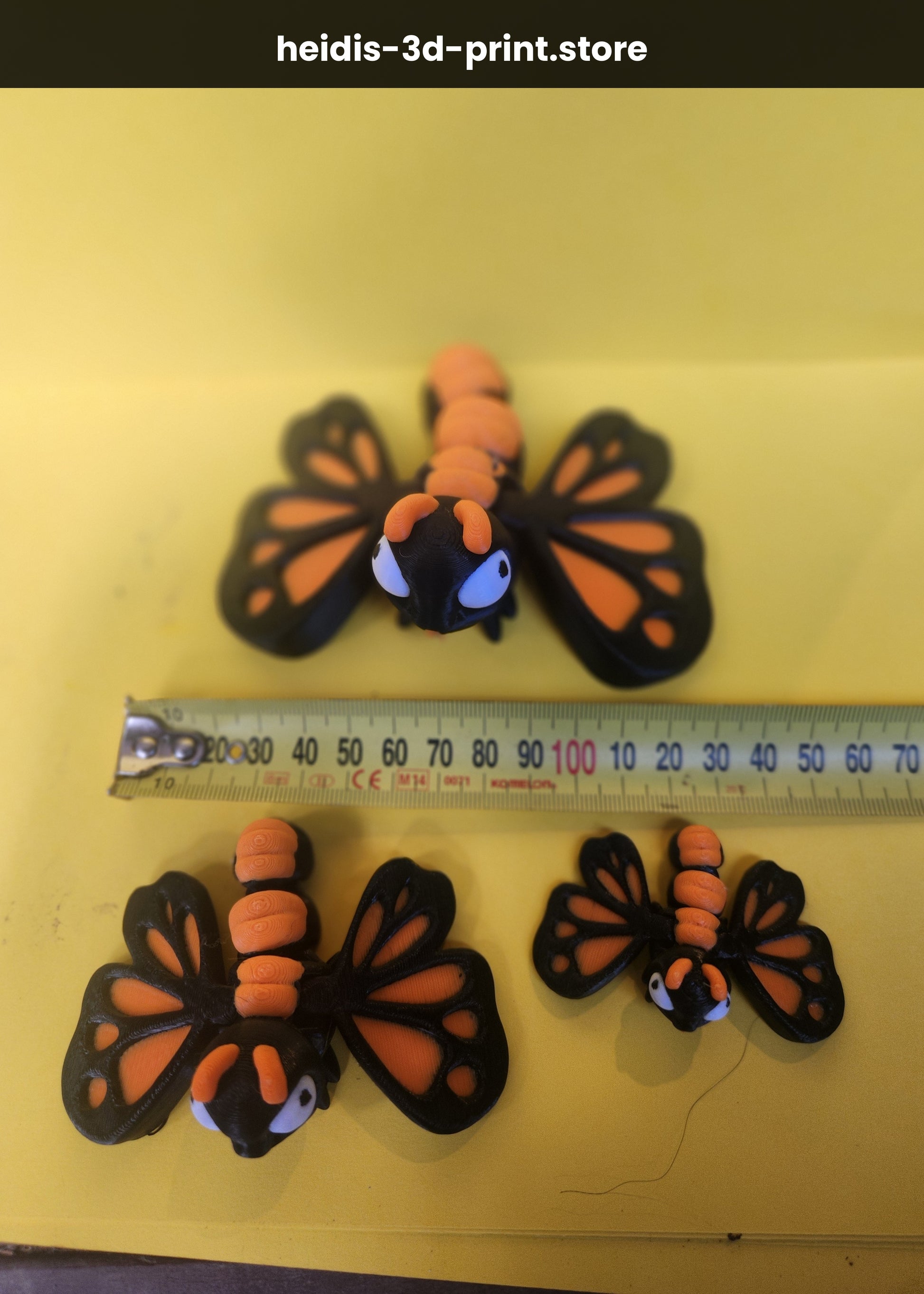 Three 3D printed cute butterfly figures on yellow background next to ruler showing size comparison, small 55mm, medium 85mm, large 115mm wide, monarch butterfly colours, Upper Hutt NZ