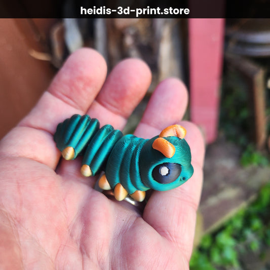 Hand holding a medium 3D printed articulated caterpillar figure in deep teal with orange accents, 28mm wide × 65mm long, showing segment detail and large expressive eye, made in Upper Hutt NZ